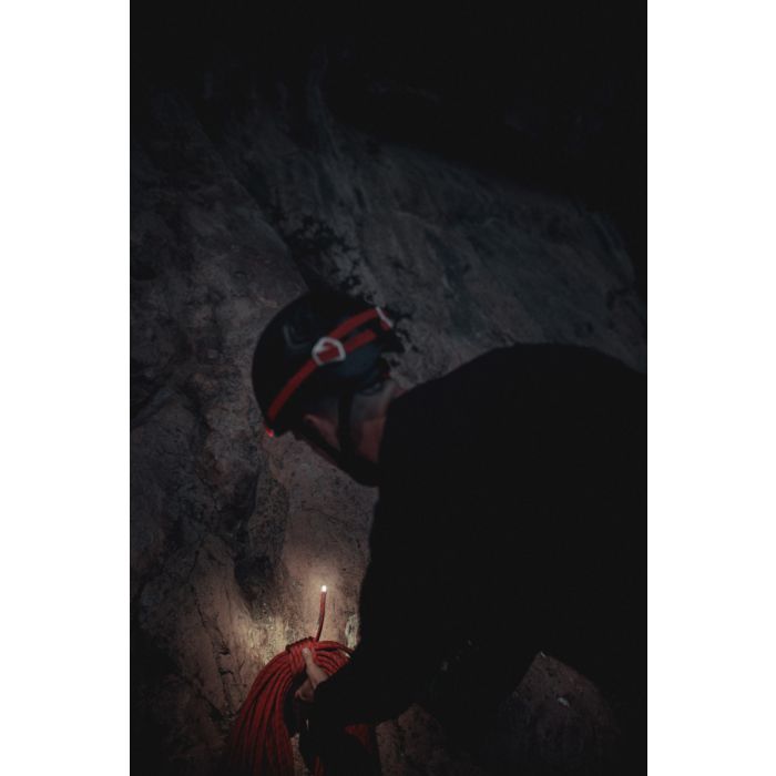 Person in a dark cave holding a rope and a flashlight