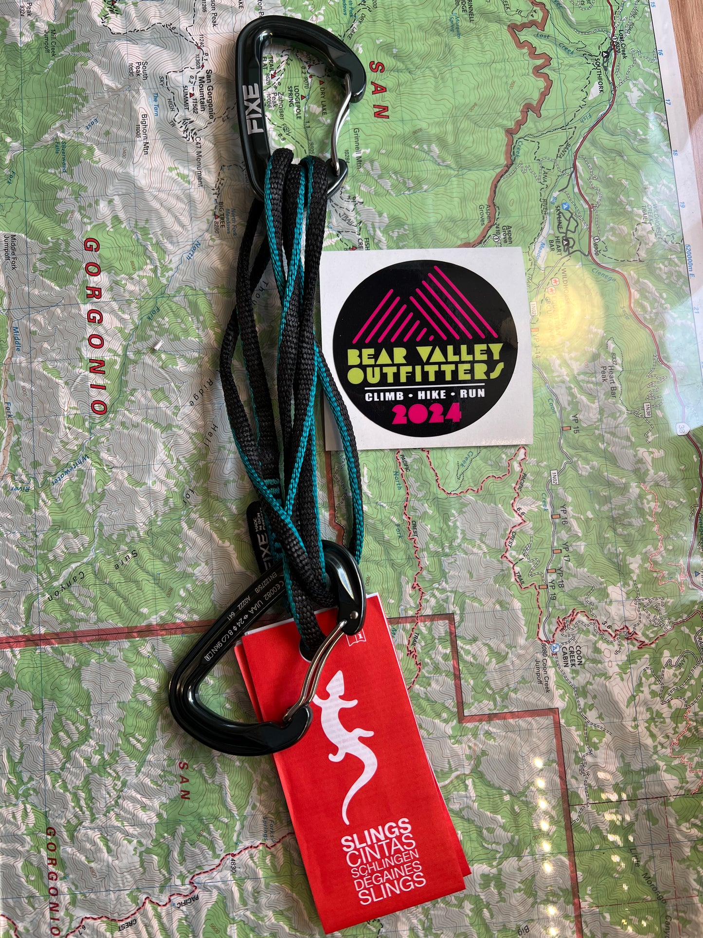 A turquoise and black climbing sling with a map and a logo of Valley Outfitters on it, placed on a map background.